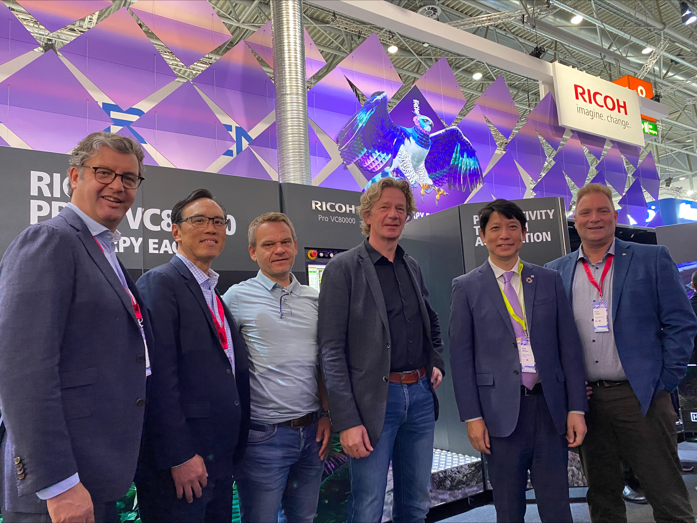 A group of men standing in front of the Ricoh sign